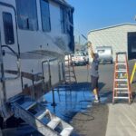 20220823_093955 Person washing a recreational vehicle outdoors.