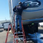 20230406_100658 Person cleaning RV logo on a ladder.